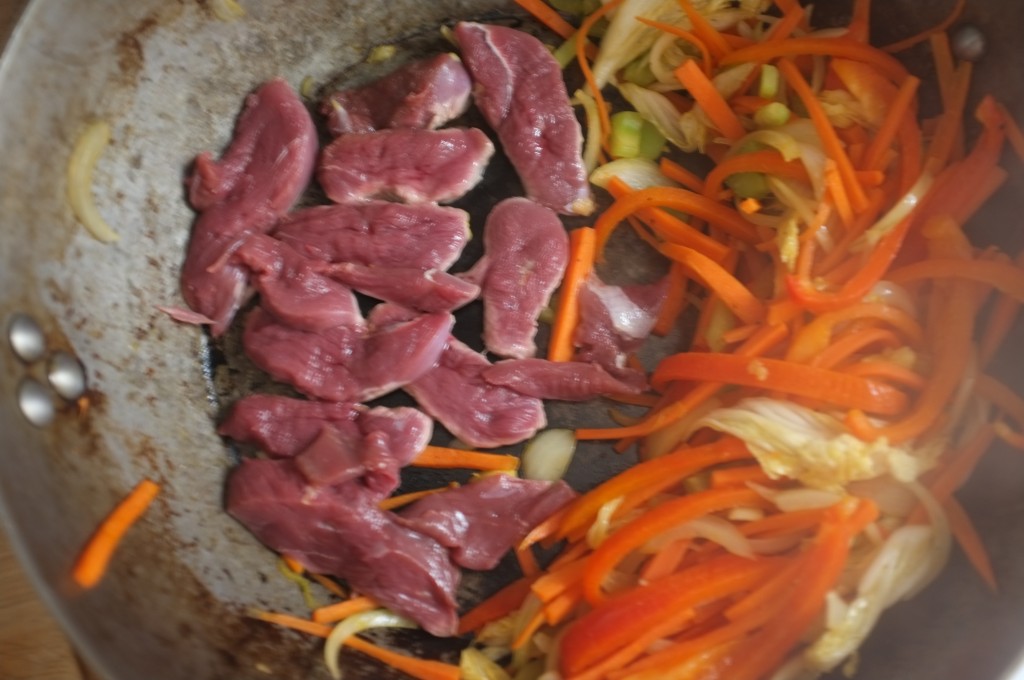 Les légumes et le canard cuisent dans le wok, on voit la vapeur qui s'échappe.